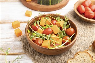 Vegetarian vegetable salad of tomatoes, pumpkin, microgreen pea sprouts on white wooden background