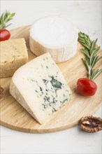 Blue cheese and various types of cheese with rosemary and tomatoes on wooden board on a white