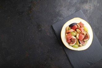 Vegetarian fruit salad of watermelon, grapes, figs, pear, orange, cashew on slate board on a black