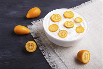 Greek yogurt with kumquat pieces in a white plate on a black wooden background, close up