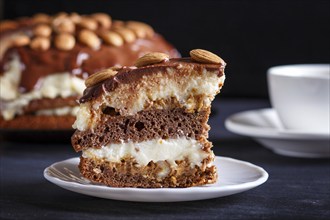 Homemade chocolate cake with milk cream, caramel and almonds on black wooden background. close up