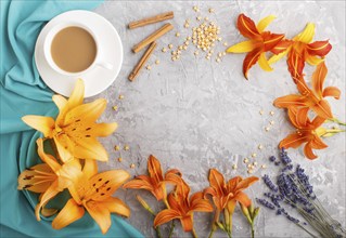 Orange day-lily and lavender flowers and a cup of coffee on a gray concrete background, with blue