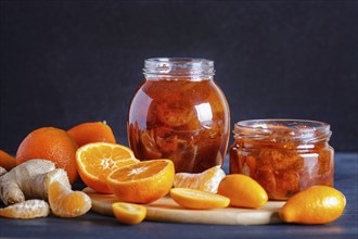 Tangerine and kumquat jam in a glass jar with fresh fruits on a black wooden table. Homemade, copy