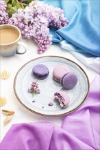 Purple macarons or macaroons cakes with cup of coffee on a white concrete background and