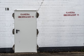 Building, industrial building, factory building, door, labelled camera monitored, symbolic image