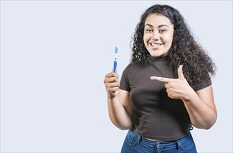 Smiling woman holding and pointing a toothbrush. Happy girl holding and pointing at toothbrush