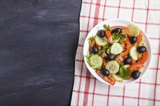 Vegetarian salad of tomatoes, cucumbers, parsley, olives and mustard on linen tablecloth and black