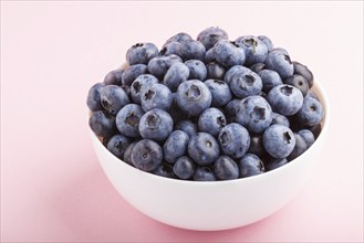 Fresh blueberry in white bowl on pink background. side view, close up