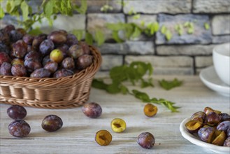 Fresh whole and sliced plums in a basket and on a white plate, on a rustic wooden table in front of