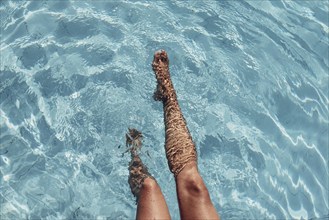 Two legs in the clear blue water of a pool, relaxed atmosphere