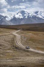 Off-road vehicle on a gravel track, glaciated and snow-covered peaks, Ak Shyrak Mountains, near