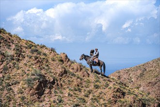 Traditional Kyrgyz eagle hunter with eagle in the mountains, hunting on horseback in front of dry