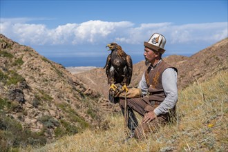 Traditional Kyrgyz eagle hunter with eagle in the mountains, near Kysyl-Suu, Kyrgyzstan, Asia