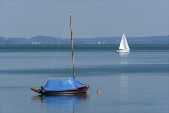 Covered and sailing boat underway on calm waters, Bernried am Starnberger See, Upper Bavaria,