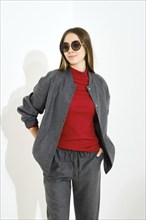 Cheerful young woman in grey tracksuit, red turtleneck and sunglasses holding hands in pockets