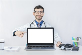 Smiling doctor pointing at an advertisement on the laptop screen. Handsome doctor pointing at an