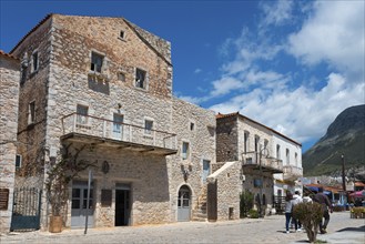 Stone buildings on a busy village street with passers-by under a blue sky with clouds, Old Town,