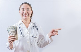 Happy female doctor holding money and pointing to side. Beautiful female doctor showing money and