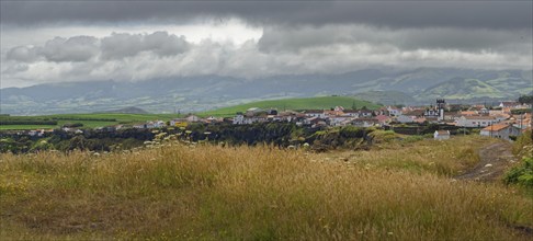 Coastal village on a hill, surrounded by green fields, under a cloudy sky, Fenais da Luz, Sao