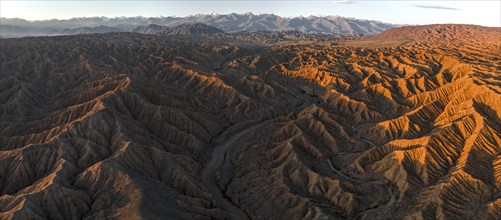 Landscape of eroded hills at Lake Issyk Kul, badlands at sunrise, mountain peaks of the Tien Shan