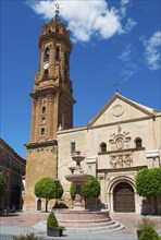 Church building with high tower and fountain on a sunny town square under a blue sky, Real