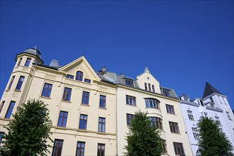 Historic Jugendstiel façade with large windows and trees in front under a clear blue sky, Bryggen,