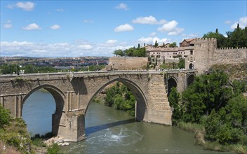 Historic stone bridge over river in rural setting with neighbouring old buildings, Puente de San