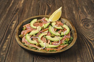 A beautifully arranged plate features slices of salmon topped with avocado, red onion, and capers,