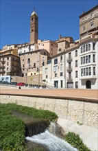 Historic town with an urban river, several buildings and a prominent tower under a clear blue sky,