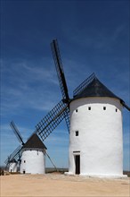 Three white windmills under a deep blue sky in a tranquil rural landscape on a sunny day, Alcazar