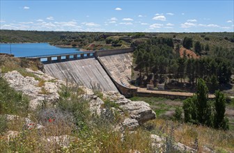 Large dam in a hilly landscape with trees and water reservoir under a clear sky, Embalse de