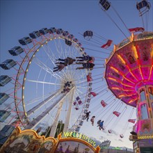 A funfair at dusk with illuminated chain carousel and Ferris wheel, Europa Rad, rides, wave flight,