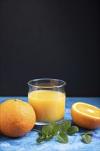 Glass of orange juice with mint on a black and blue background. Hard light, contrast. Side view,