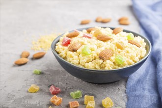 Millet porridge with candied fruits and almonds in blue ceramic bowl on a gray concrete background