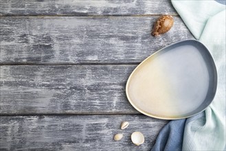 Empty blue ceramic plate on gray wooden background and blue textile. Top view, copy space, flat lay