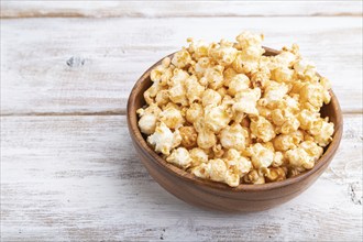 Popcorn with caramel in wooden bowl on a white wooden background. Side view, close up