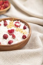 Rice flakes porridge with milk and strawberry in wooden bowl on gray wooden background and linen