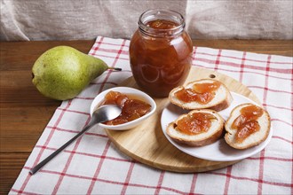 Pear jam in a glass jar on a linen tablecloth on a wooden table. Homemade, copy space