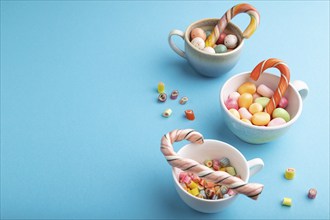 Heap of multicolored caramel candies in cups on blue pastel background. copy space, side view