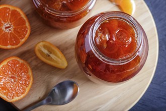 Tangerine and kumquat jam in a glass jar with fresh fruits on a black wooden table. Homemade, close