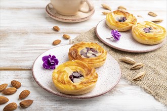 Small cheesecakes with jam and almonds with cup of coffee on a white wooden background and linen