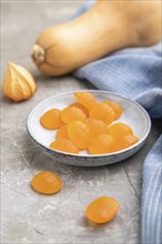 Jelly pumpkin candies on gray concrete background and blue linen textile. close up, side view,