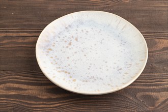 Empty blue and gold ceramic plate on brown wooden background. Side view, copy space