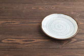 Empty blue ceramic plate on brown wooden background. Side view, copy space