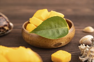 Dried and candied mango cubes in wooden bowls on brown wooden textured background. Side view, close