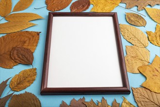 Composition with yellow and brown autumn leaves and wooden frame mockup on blue pastel background.