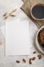 White paper invitation card, mockup with almonds, bun, cup of coffee, linen textile on gray