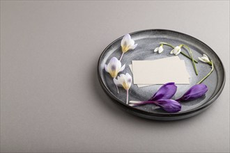 Gray paper invitation card, mockup with crocus and galanthus flowers on ceramic plate and gray