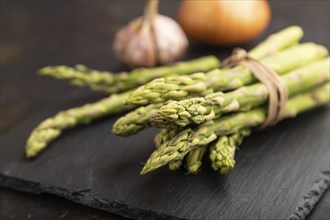 Bunch of fresh green asparagus, garlic, onion on slate board on black concrete background. Side