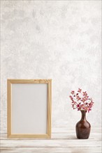 Wooden frame with purple barrenwort flowers in ceramic vase on gray concrete background. side view,